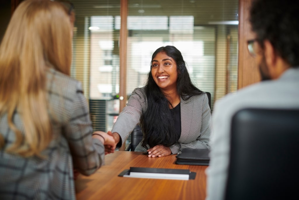 Young woman shaking hands across table with another woman during law firm interview